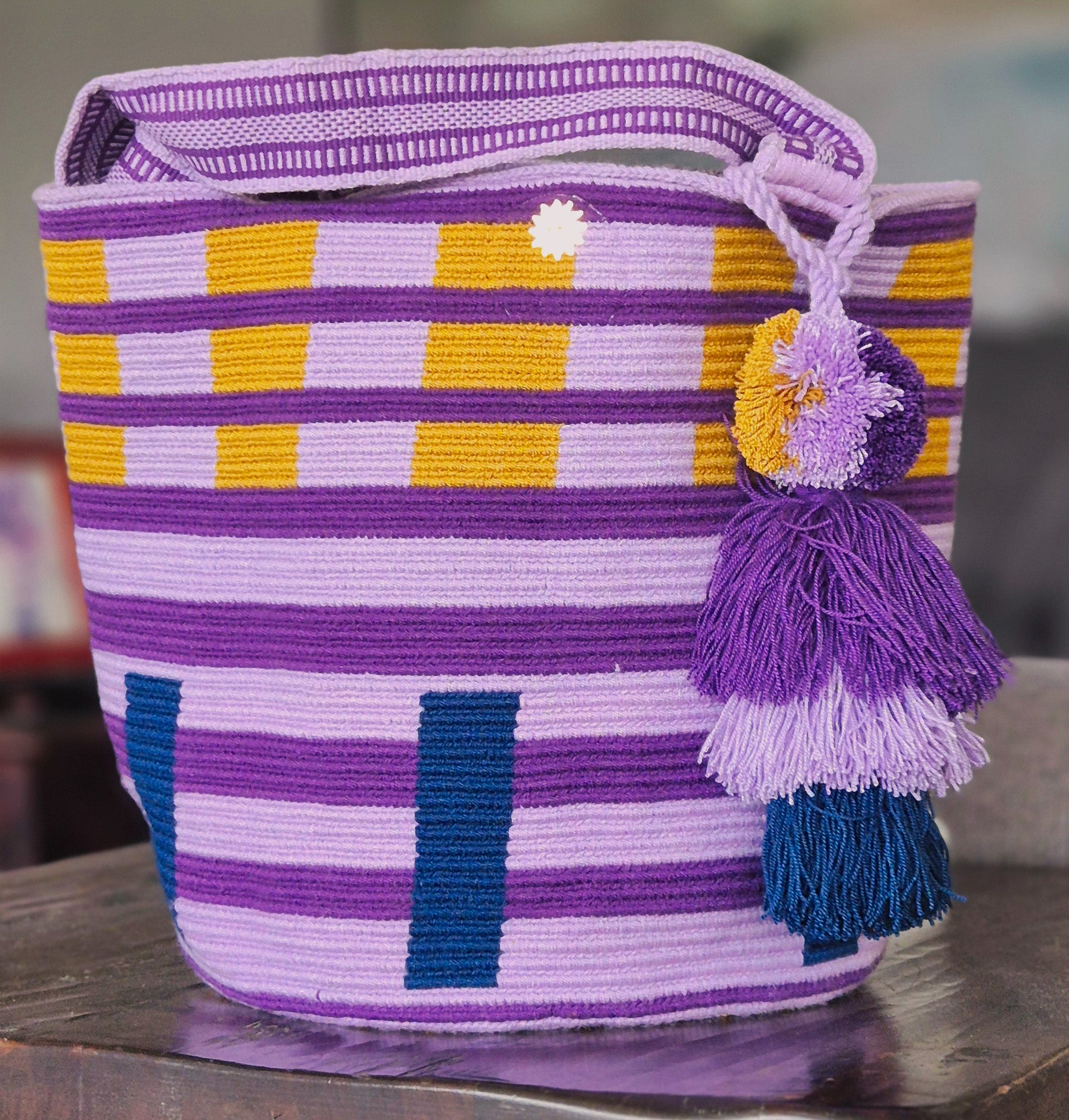Cartera violeta, lineas moradas, cuadros en mostaza y azul con asa y pompón en igulaes colores