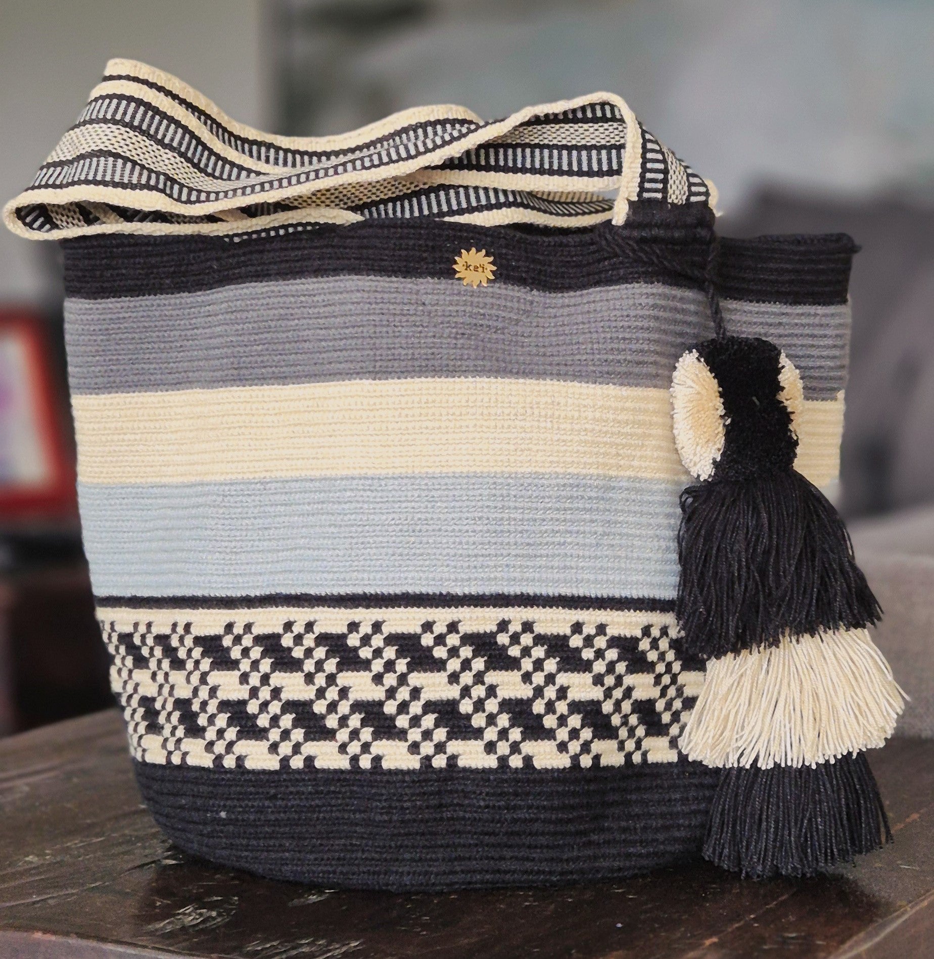 Purse with gray, beige, light blue, black stripes and diagonal pixel pattern with handle and pompom in matching colors