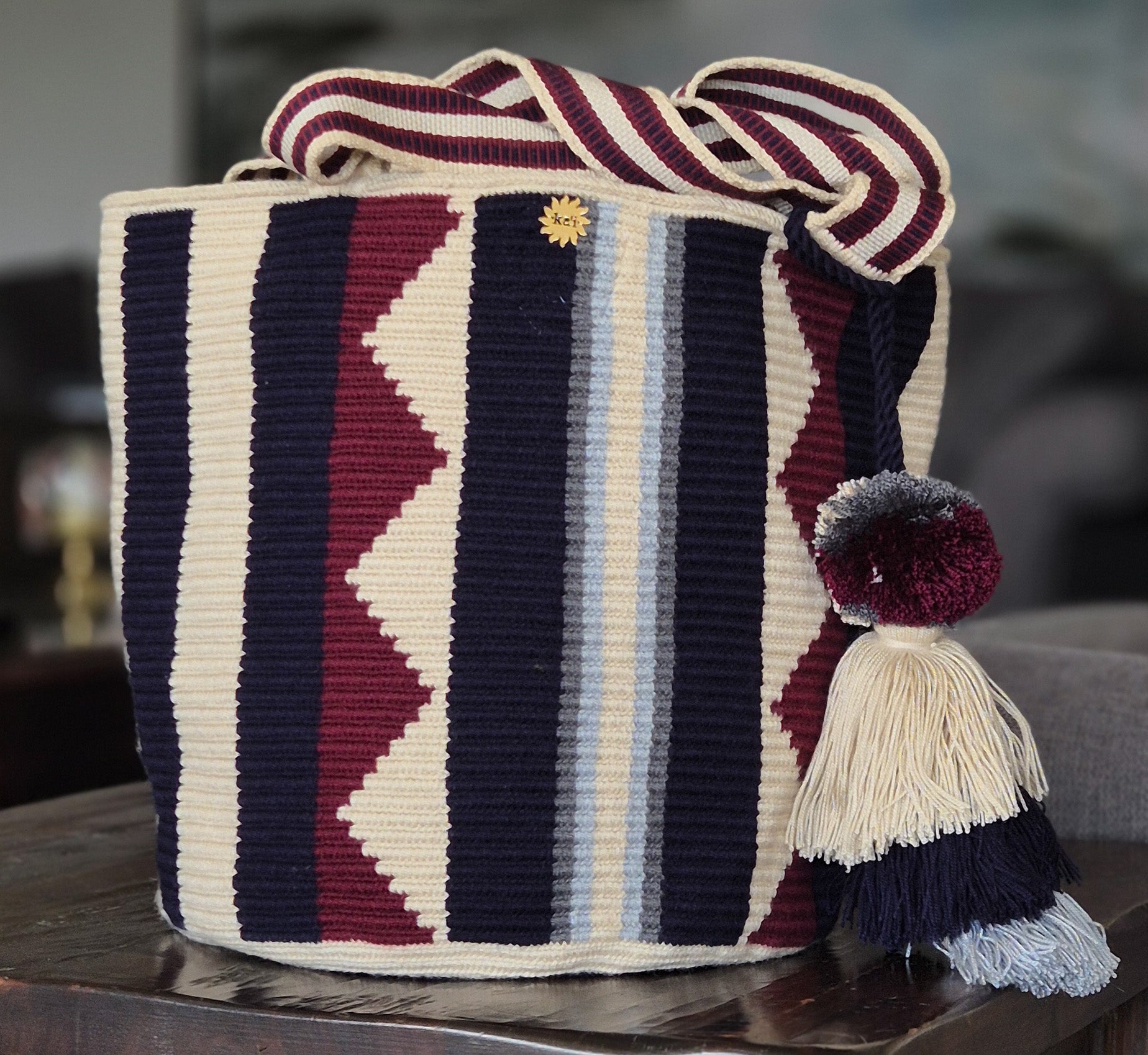 Cartera a bandas gris, beige, azul claro, negro y triangulos en vino tinto con asa y pompón en iguales colores